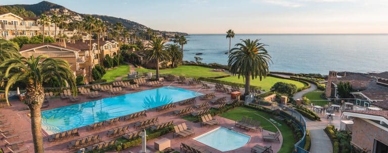 a pool with lounge chairs and palm trees by the ocean - Laguna Beach