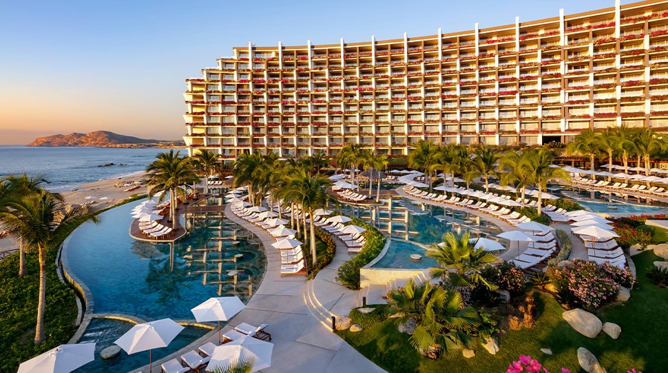 Aerial view of a luxury oceanfront resort with tiered infinity pools, palm trees, and sunset lighting — showcasing high-end hospitality design and destination appeal