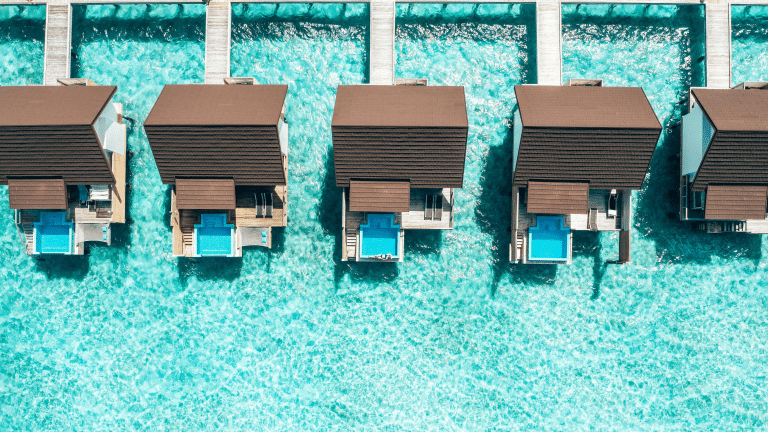 Aerial view of luxury overwater resort villas with private plunge pools set above clear turquoise ocean water.