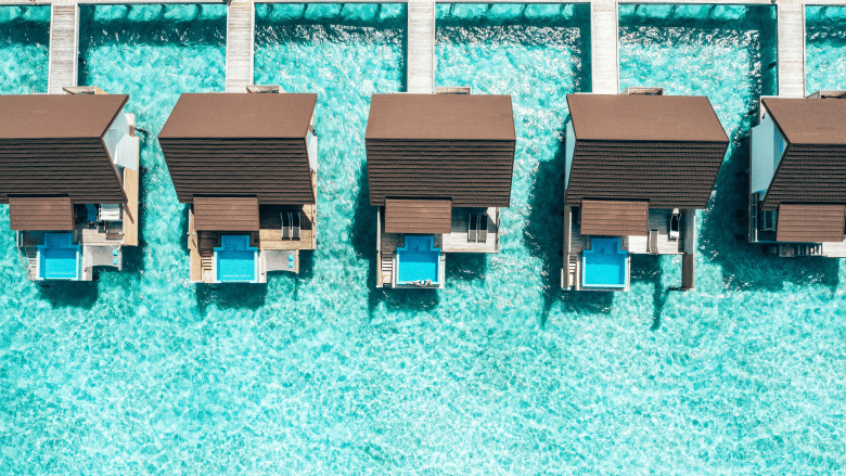 Aerial view of luxury overwater resort villas with private plunge pools set above clear turquoise ocean water.